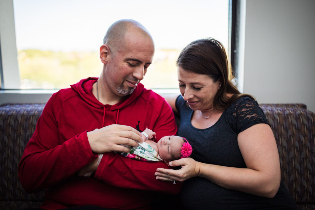 Two new parents look down at their newborn baby during a fresh 48 newborn photography session.