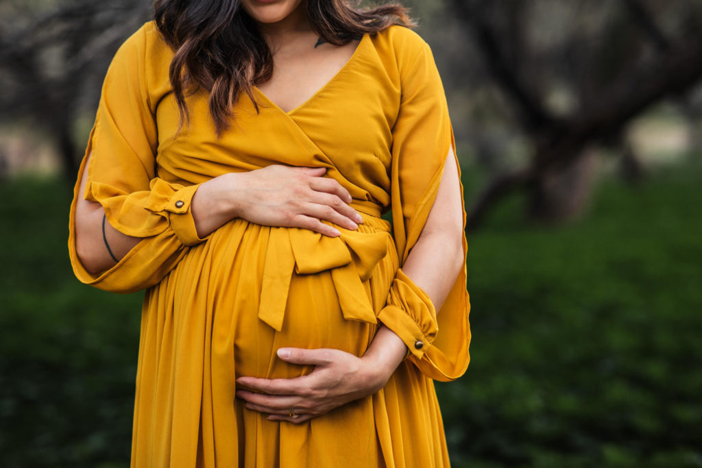 Maternity Photography in Mesa AZ - A pregnant mother hugs her belly outdoors in a vibrant yellow dress.