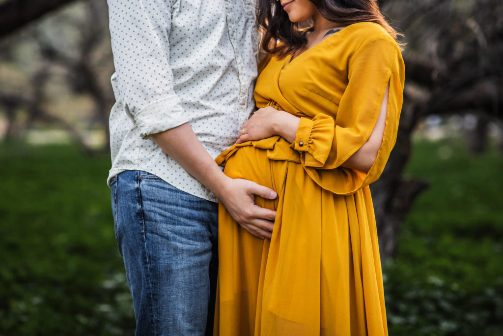 Maternity Photography in Mesa AZ - A pregnant mother looks down as her husband rests his hand on her belly.