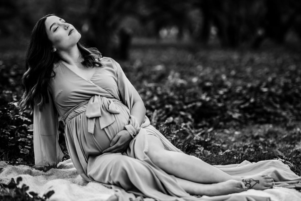 A pregnant mother laying in a field of greenery with her eyes closed and pointed up toward the sky.